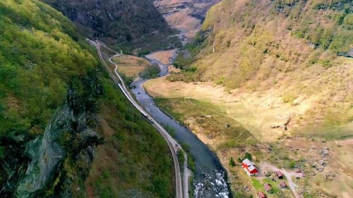 A river flowing through a steep valley with a train on the railroad tracks - aerial view