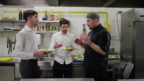 Side View of a Professional Chef in a Black Uniform Communicating with Two Waiters in White Shirts