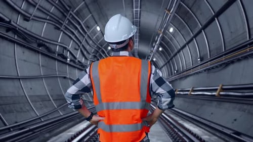 Rückansicht eines männlichen Ingenieurs, der sich mit Waffen umschaut Akimbo im U-Bahn-Tunnel