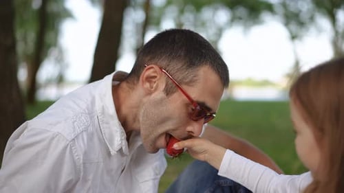 Father and Daughter Eating Strawberry Together at Park