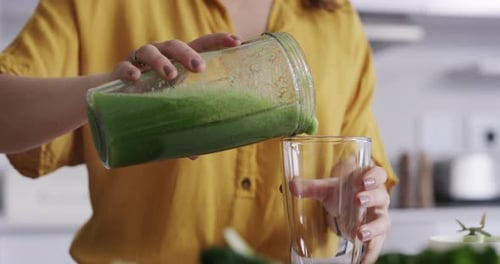 Woman Pours Green Smoothie in Bright Kitchen