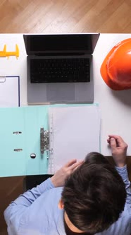 Vertical Video Engineer Sitting at an Office Desk Working on a Laptop Computer Reviewing
