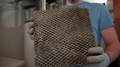 Worker HVAC Services Changing a Folded Dirty Air Filter in the HVAC Furnace System in Home
