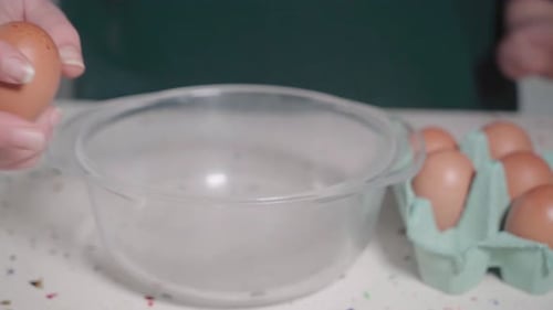 Frau knackt Ei mit einer Hand an der Seite einer Glasschale, Nahaufnahme