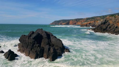 Sunny Rocky Coastal Landscape with Blue Sea Splashing on Rough Cliffs Aerial