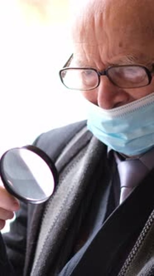 Senior Man Looking Through Magnifying Glass Wearing Mask