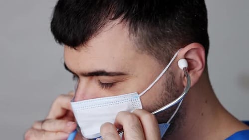 portrait of male doctor with surgical mask is putting stethoscope in ears