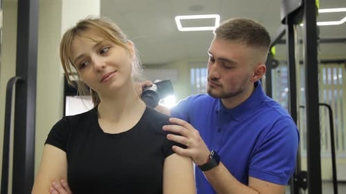 A Man is Helping a Woman Stretch Her Neck in a Gym