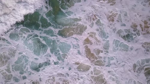 Top down aerial of foamy ocean waves hitting the rocks