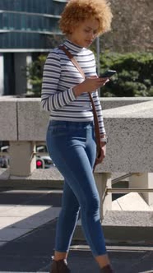 Vertical video: Woman stepping past concrete parapet while tapping smartphone on skywalk