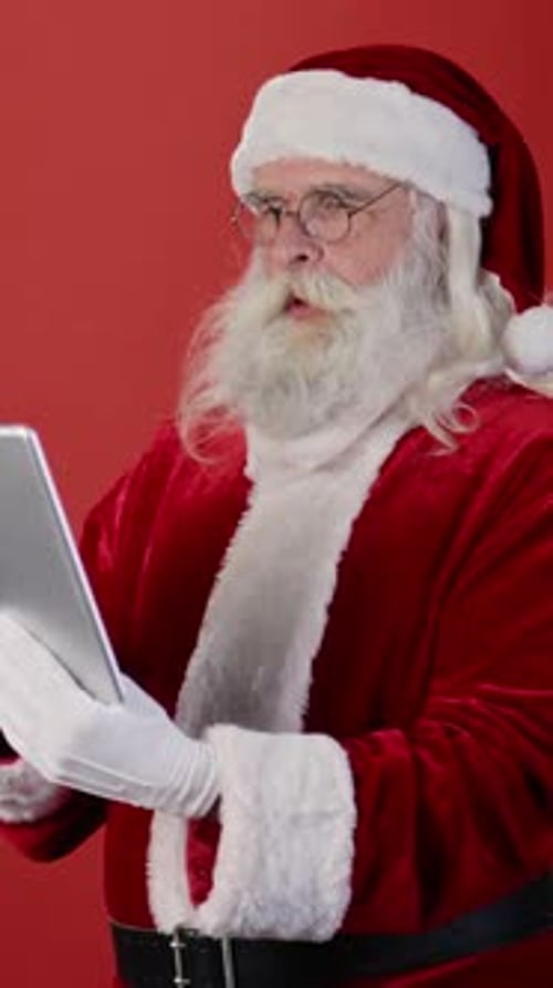 Santa Claus Typing on Tablet Against Red Background