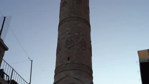 The camera scans the minaret of the historic Mardin Ulu Mosque, made of cut stone, from the bottom u