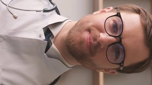 Portrait of a Handsome Young Doctor in a White Uniform and Glasses Standing on a Background