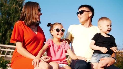 Young Happy Family Sitting in the Park on a Sunny