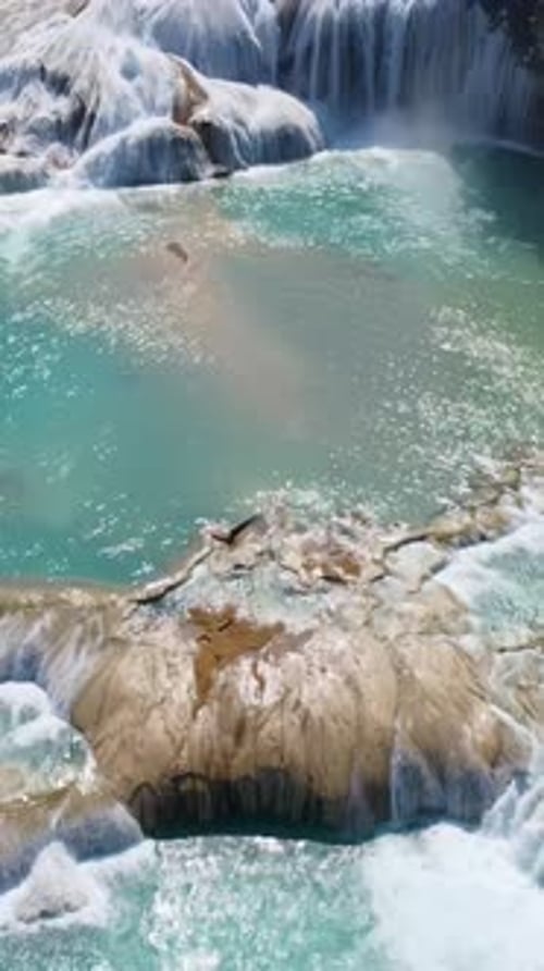 Aerial drone view multiple turquoise waterfalls and natural pools surrounded by dense tropical fores