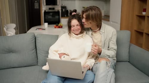 Couple Sitting on Couch Laughing at Laptop