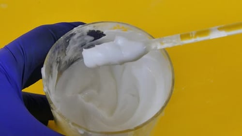 Gros plan des mains d'un chimiste dans des gants bleus mélangeant une émulsion cosmétique dans un laboratoire