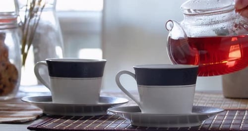 Teekanne gießt Tee in eine Tasse