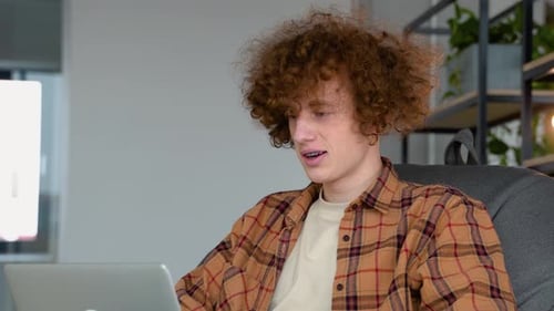 Young Man with Curly Hair Uses Laptop Indoors