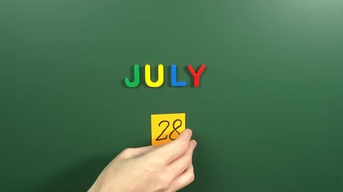 Hand sticking a sticker 28 July calendar day on school board. 28 date of July. Twenty eighth day
