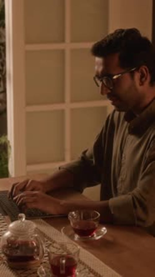 Vertical d'un Indien portant des lunettes travaillant en ligne à la maison en soirée