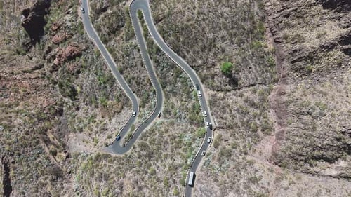 Top-down drone fly over winding mountain road with cars navigating safely sharp bends in dry rocky