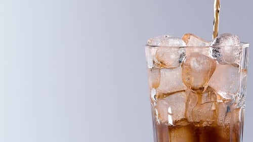 Pouring cola drink with ice cubes close-up.
