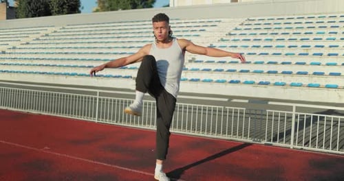 Young African American Man Warming Up and Stretching Before Workout or Jogging on Running Track at