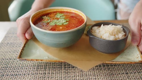 Tom Yam soup close-up, Asian cuisine. Hand of waiter puts Thai traditional dish on table