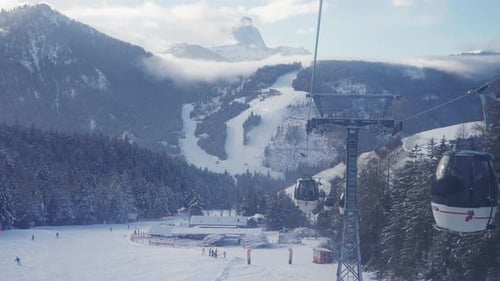 Ski Lift Ascends Over Snowy Alpine Forest With Mountain Panorama and Sun Rays in the Dolomites