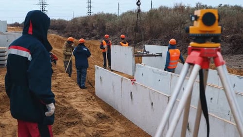 Un topógrafo que usa un teodolito toma medidas del área en un sitio de construcción industrial