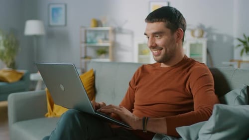 Smiling man typing on a laptop at home
