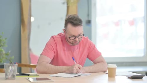 Man Writing in Notebook at Desk in Office
