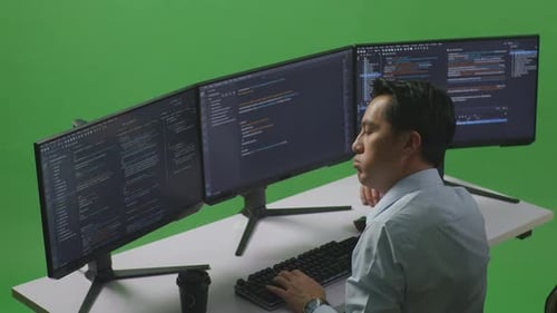 Side View Of Bored Asian Man Developer Write Code With Multiple Computer Screens In Green Screen