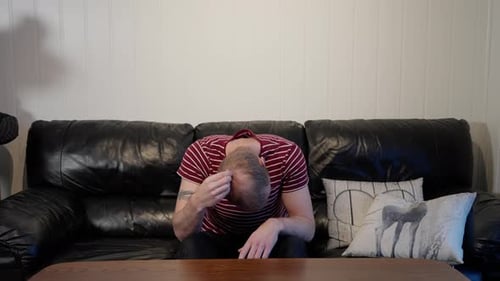Middle aged man in sofa frustrated about hair loss, shakes head