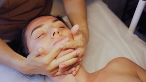 Woman receiving facial massage on examination bed