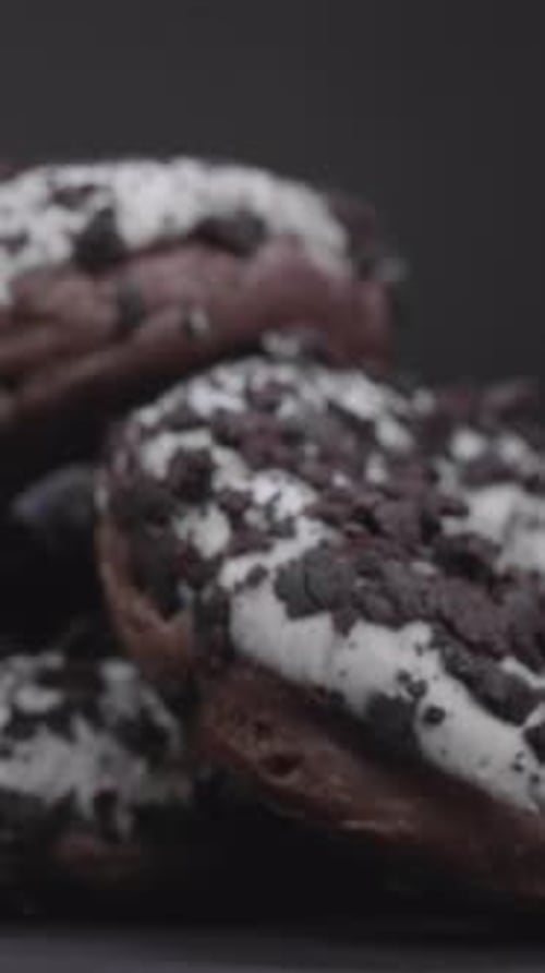 Close-up vertical shots of chocolate donuts with white topping against black background