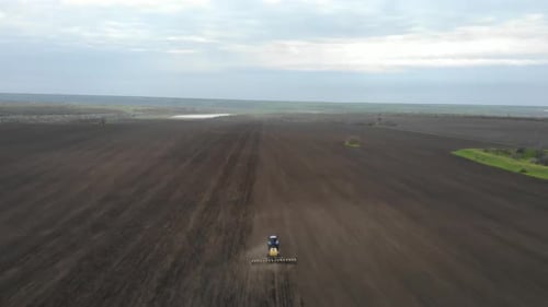 Blue tractor planting sunflower with yellow planter on the field in Ukraine