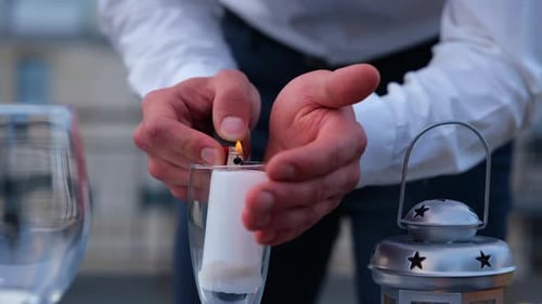 Close Up of Man Hands Lighting Candles Outdoors on a Table Preparing Romantic Date Surprise Dinner