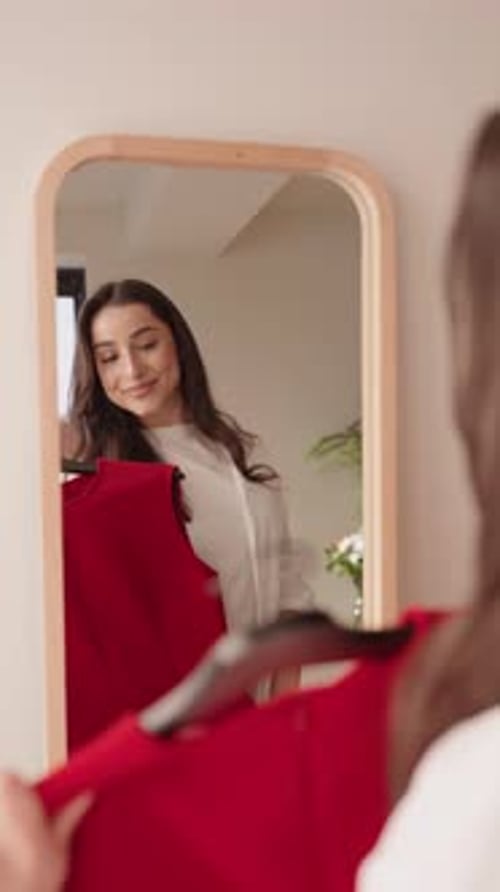 Jovem mulher experimentando um vestido vermelho olhando no espelho