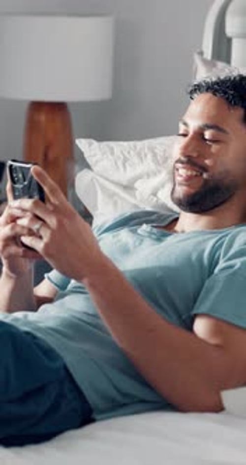 Smiling Man Lying in Bed Using Mobile Phone
