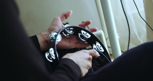 Young man's hands playing a black tambourine in a soft rhythm in a room. 4K.