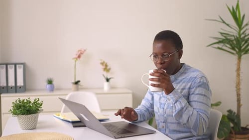 Young african american man uses a laptop for work while drinking coffee in his modern home office