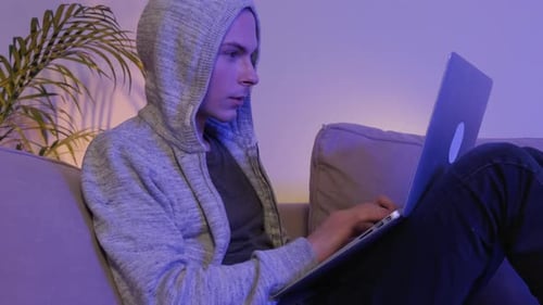Ein Mann mit Interesse spielt abends auf einem Laptop und liegt zu Hause auf der Couch