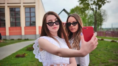 Two Girls Schoolgirls Make a Selfie Using a Smartphone Against the Background of the School