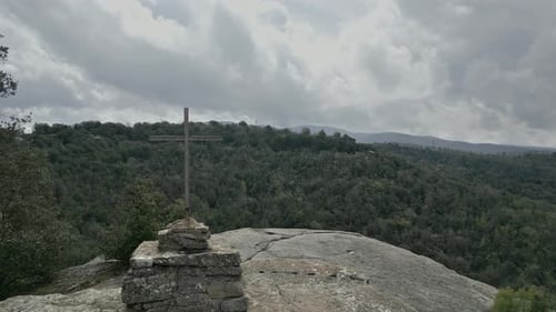 Metal cross stands on rocky mountain peak overlooking vast forest