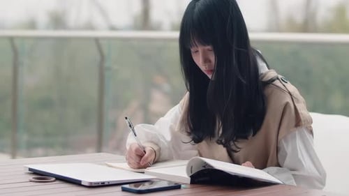 Portrait of happy joyful pretty female student busy hard working sitting against background of books