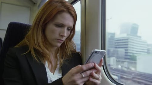 Commuter on her way to work looking out of the window and using smart phone