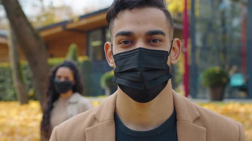 Hispanic Man in Medical Face Mask Looking at Camera Posing in Foreground in City Autumn Park