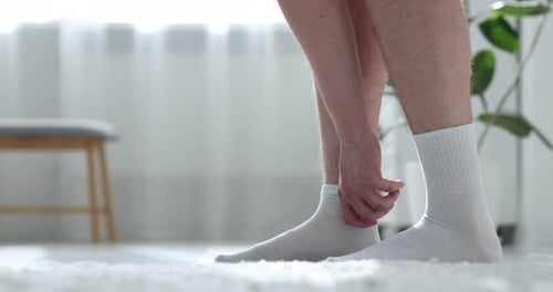 Man Puts On White Socks Inside Airy Apartment